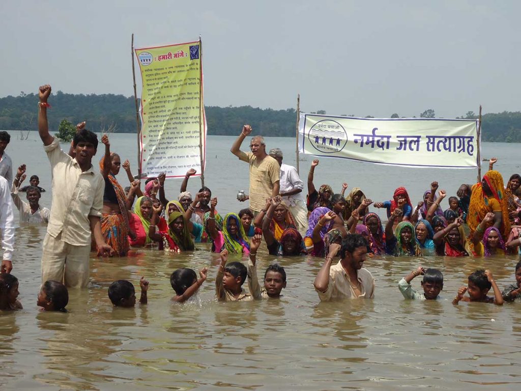 Protestors stand in rising waters to demand full rehabilitation of affected communities